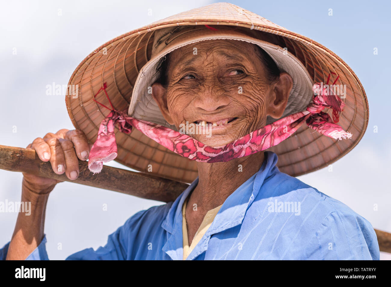 Hoi An, Vietnam - October 28, 2018: a smiling elderly Vietnamese lady, a street vendor, poses in a conical hat. Stock Photo