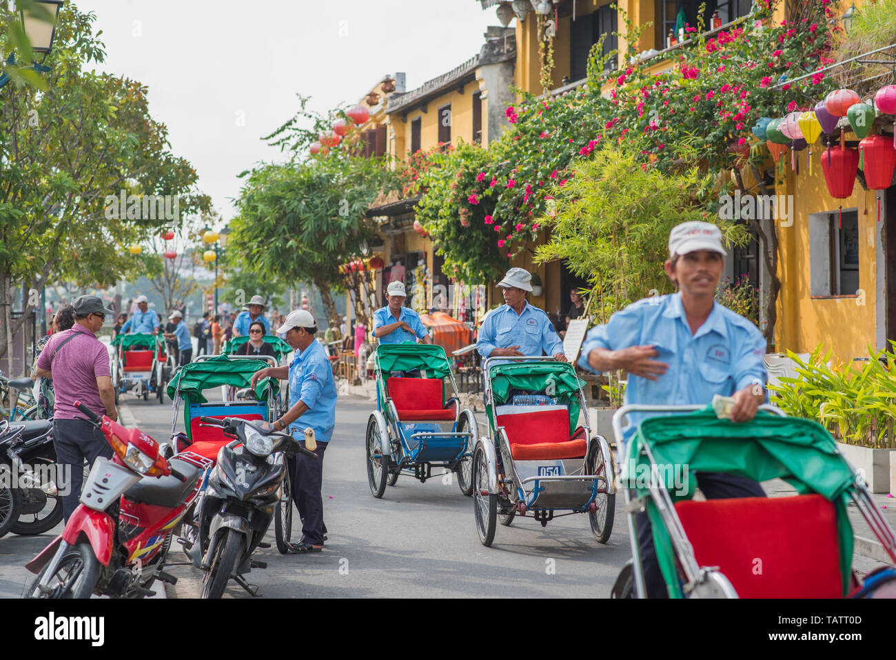 Hoi An, Vietnam - October 28, 2018: the old town's street with its rickshaws, yellow houses, lanterns, lush vegetation, and flowers. Stock Photo