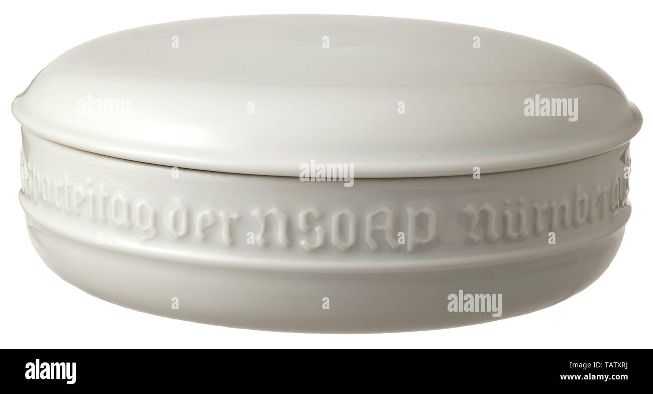 A bivouac bowl 1936, White glazed porcelain with surrounding inscription in relief 'Biwak-Abend der SS - Reichsparteitag der NSDAP Nürnberg 1936' (tr. 'Bivouac Evening of the SS - Reich Party Rally of the NSDAP Nuremberg 1936') between meandering bands, complete with lid. Green underglaze manufactory mark 'SS Allach' within an octagon surrounded by the stamped inscription 'SS. Porz - Manufr - Allach München'. Diameter 13.5 cm, height 5.5 cm. In black, velvet lined present box. Rare. porcelain, chinaware, historic, historical 20th century, Editorial-Use-Only Stock Photo