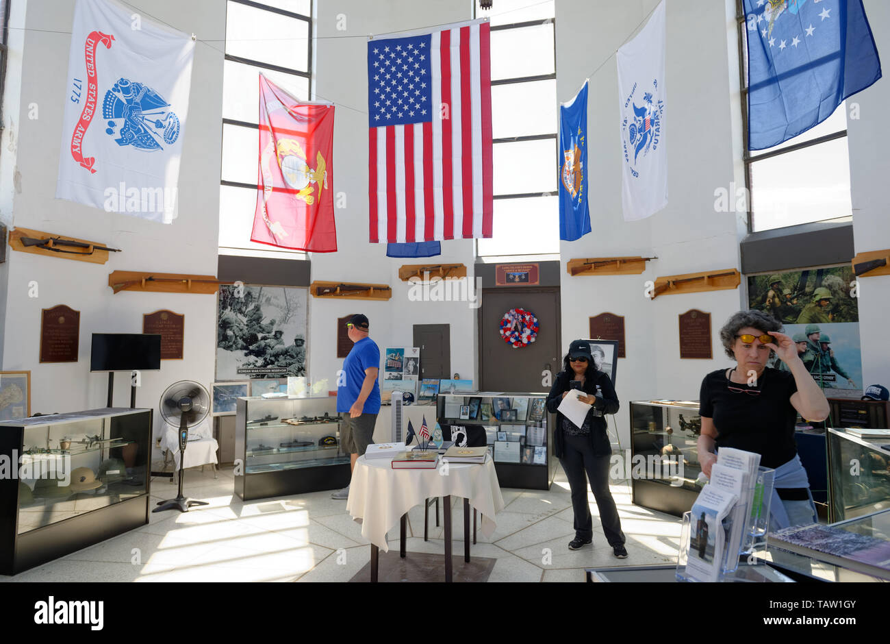 East Meadow, New York, USA. 25th May, 2019. Visitors at the Nassau County Veterans Memorial Museum look at miliary memorabilia displayed under the American Flag and military flags of the United States Armed Forces - Army, Navy, Marine Corps, Air Force, Coast Guard - suspended high in the ceiling, during Saturday of Memorial Day Weekend at Eisenhower Park on Long Island. Credit: Ann Parry/ZUMA Wire/Alamy Live News Stock Photo
