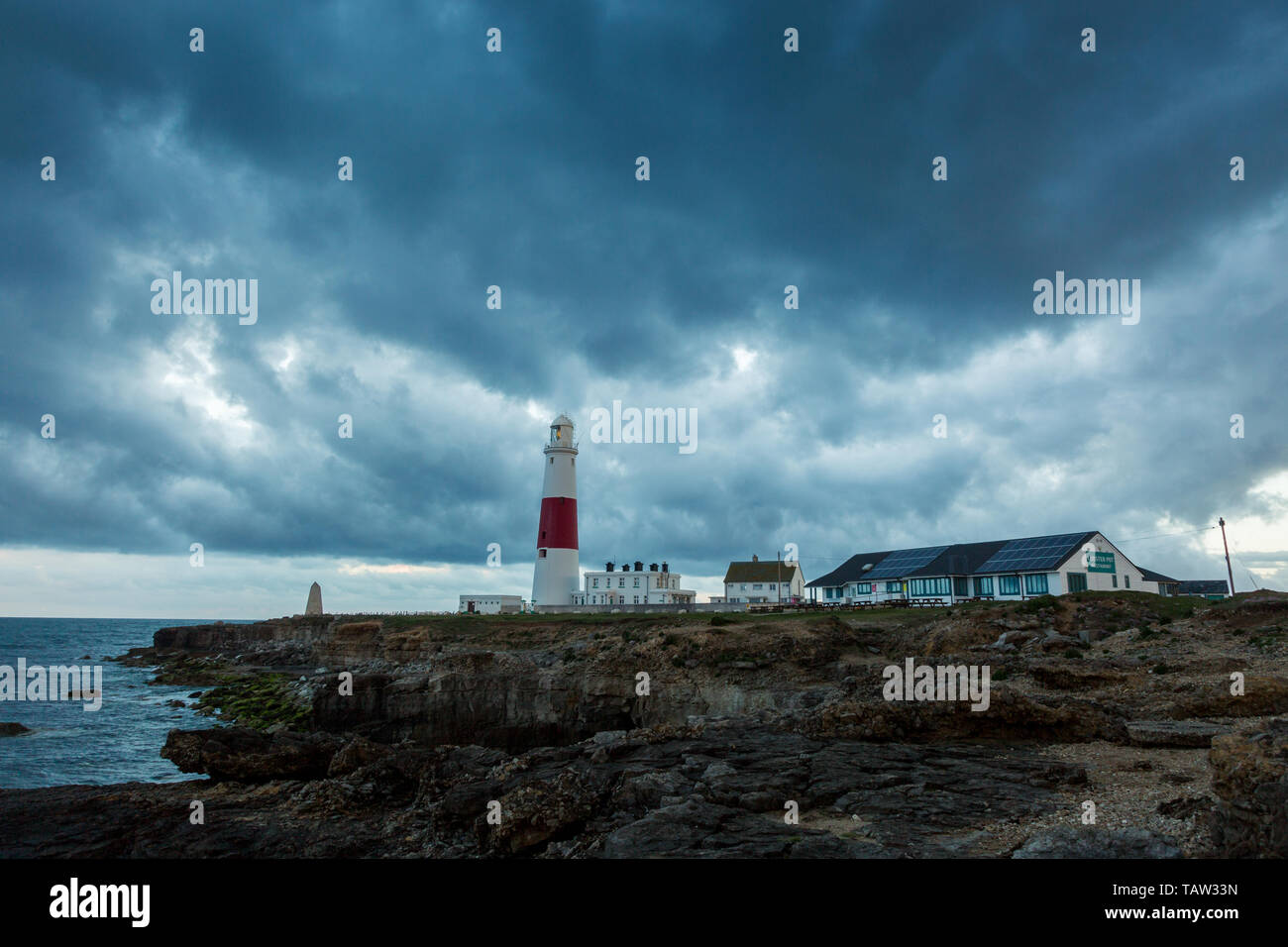 Portland, Dorset, UK. 28th May, 2019. Dramatic rain clouds fill the sky as dawn breaks at Portland Bill lighthouse, Dorset. The cloud and sun begin a day of unsettled weather. Peter Lopeman/Alamy Live News Stock Photo