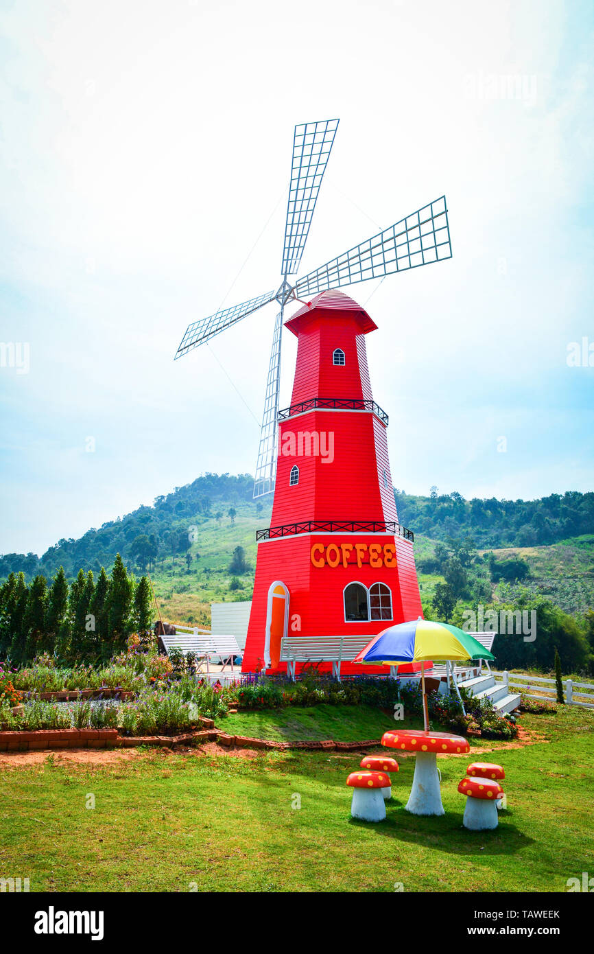 Red windmill wind turbine in the garden park with colorful umbrella on bench - coffee shop outdoors and hill background Stock Photo