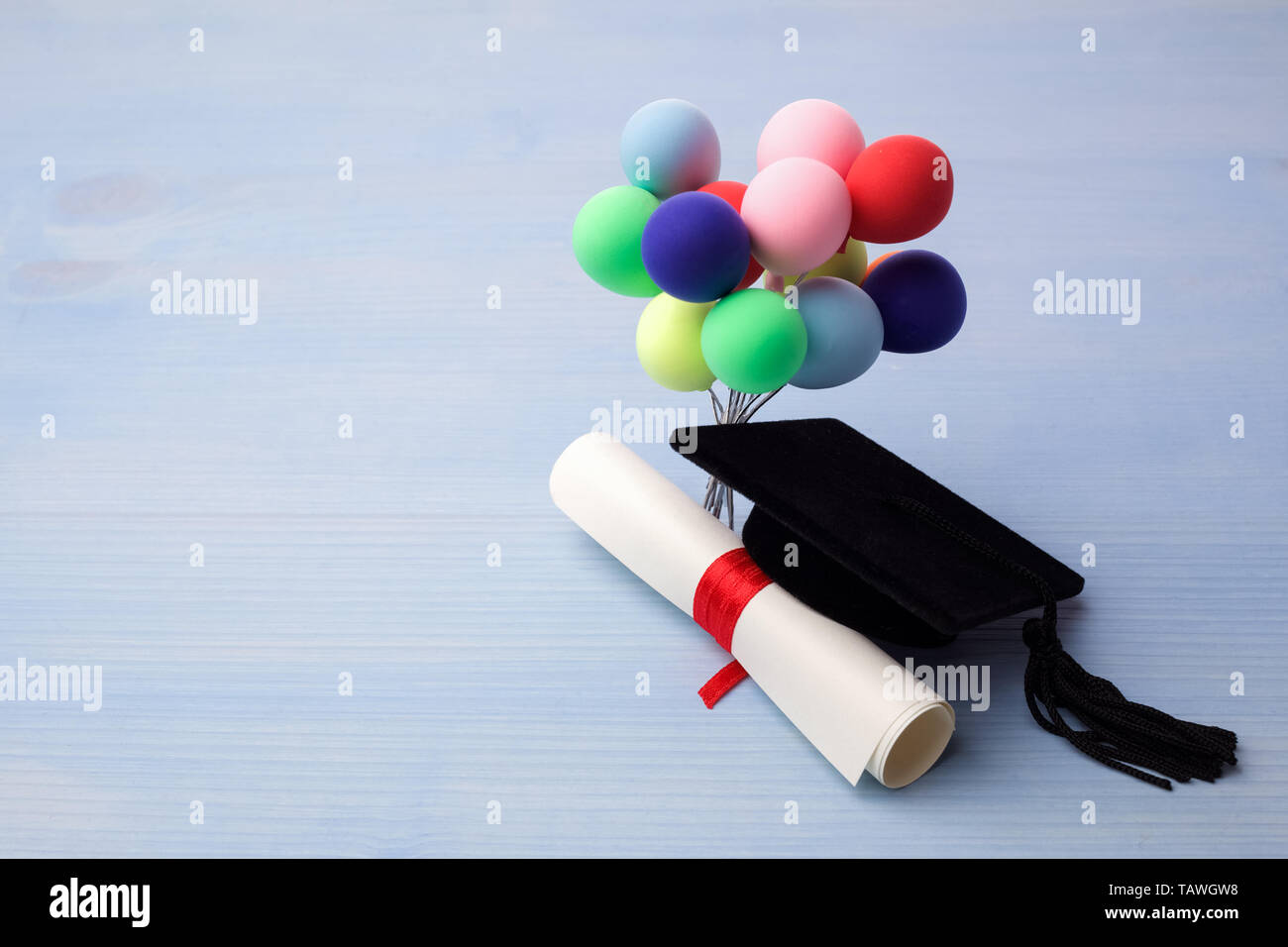 Black Graduation Cap, Degree and balloons on light blue Wooden Background. Stock Photo