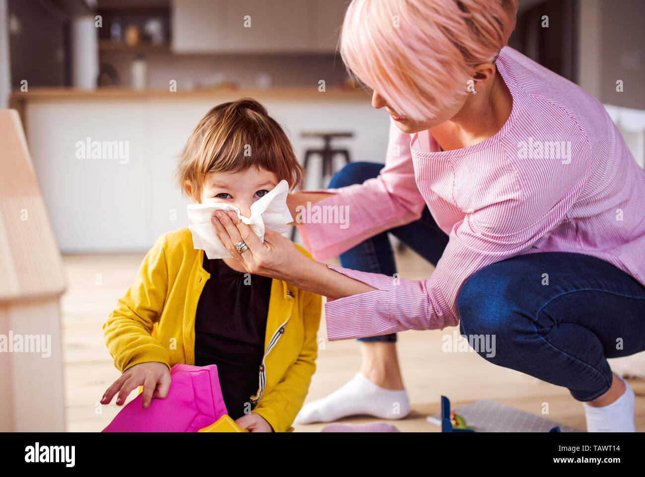 Mother blowing her small daughter's nose when playing at home. Stock Photo