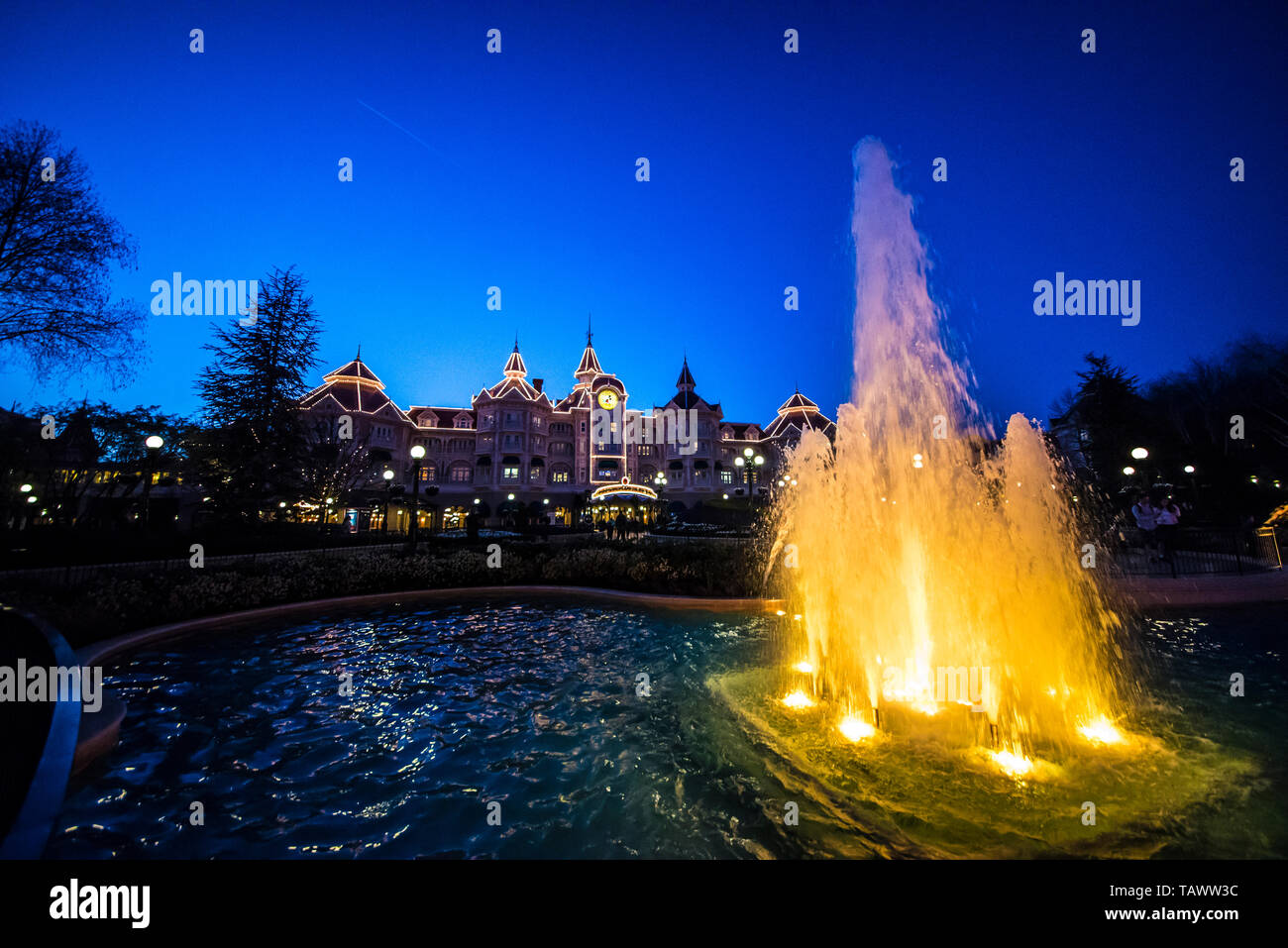 Illuminated fountain outside the entrance to Disneyland Paris. Disney Hotel, Disneyland Hotel at twilight at blue hour. Water Stock Photo