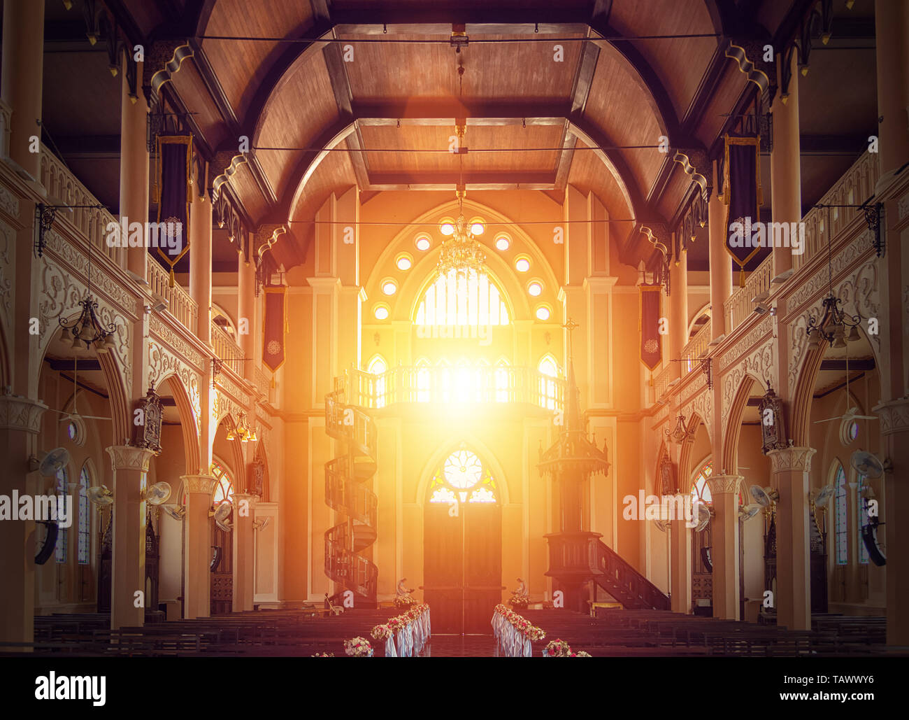 interior view of empty church with wooden bench decorated with flower bouquet, sunlight through church stained glass window Stock Photo