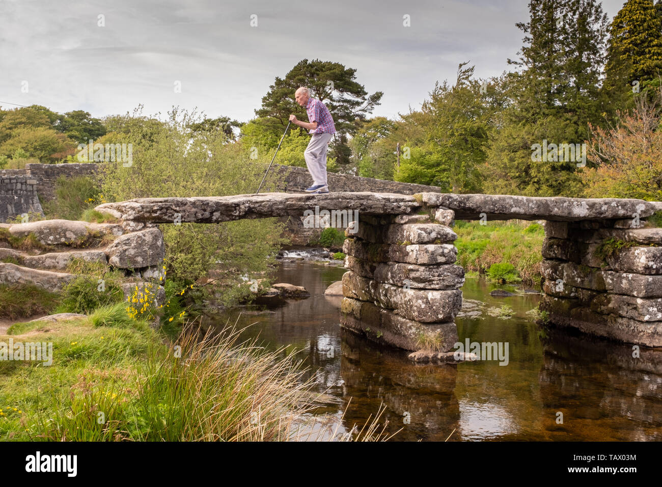 Elderly man crossing the medieval clapper bridge at Postbridge, Dartmoor, Devon, UK Stock Photo
