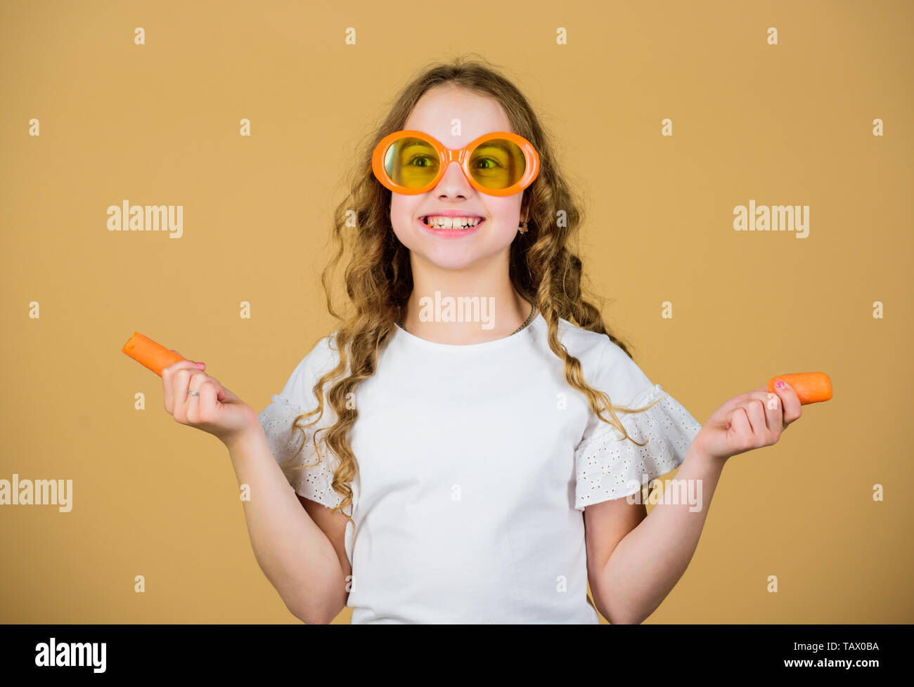 happy girl eat fresh carrot. summer vacation. little girl in fashion glasses. Vitamin nutrition. refreshing vitamin juice. Health care. Summer vitamin diet. Natural vitamin source. Vegetarian concept. Stock Photo
