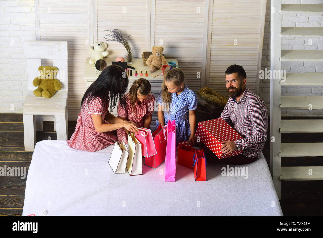 Celebration and shopping concept. Mother, father and daughters with shopping bags and packs. Family with cheerful faces open presents at home. Man, wo Stock Photo