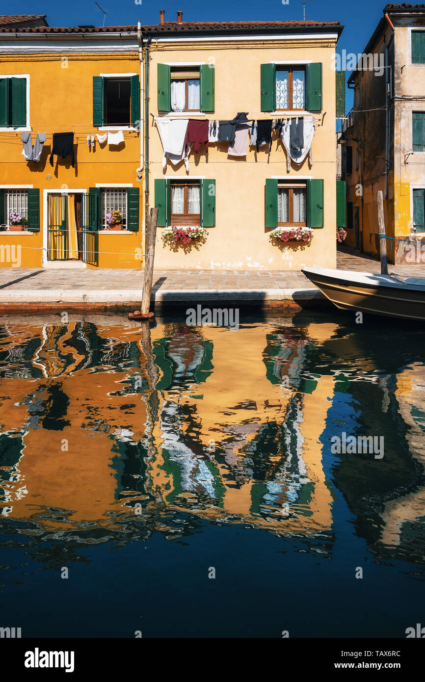 Laundry dries on the facades of colorful houses with reflection in canal, Burano, Venice, Italy Stock Photo