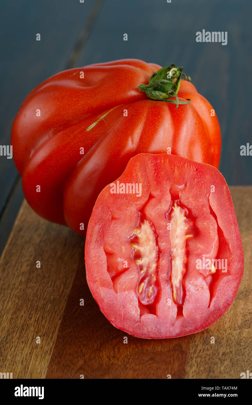 Large freshly harvested whole and sliced oxheart tomatoes. Dark wooden table, high resolution Stock Photo