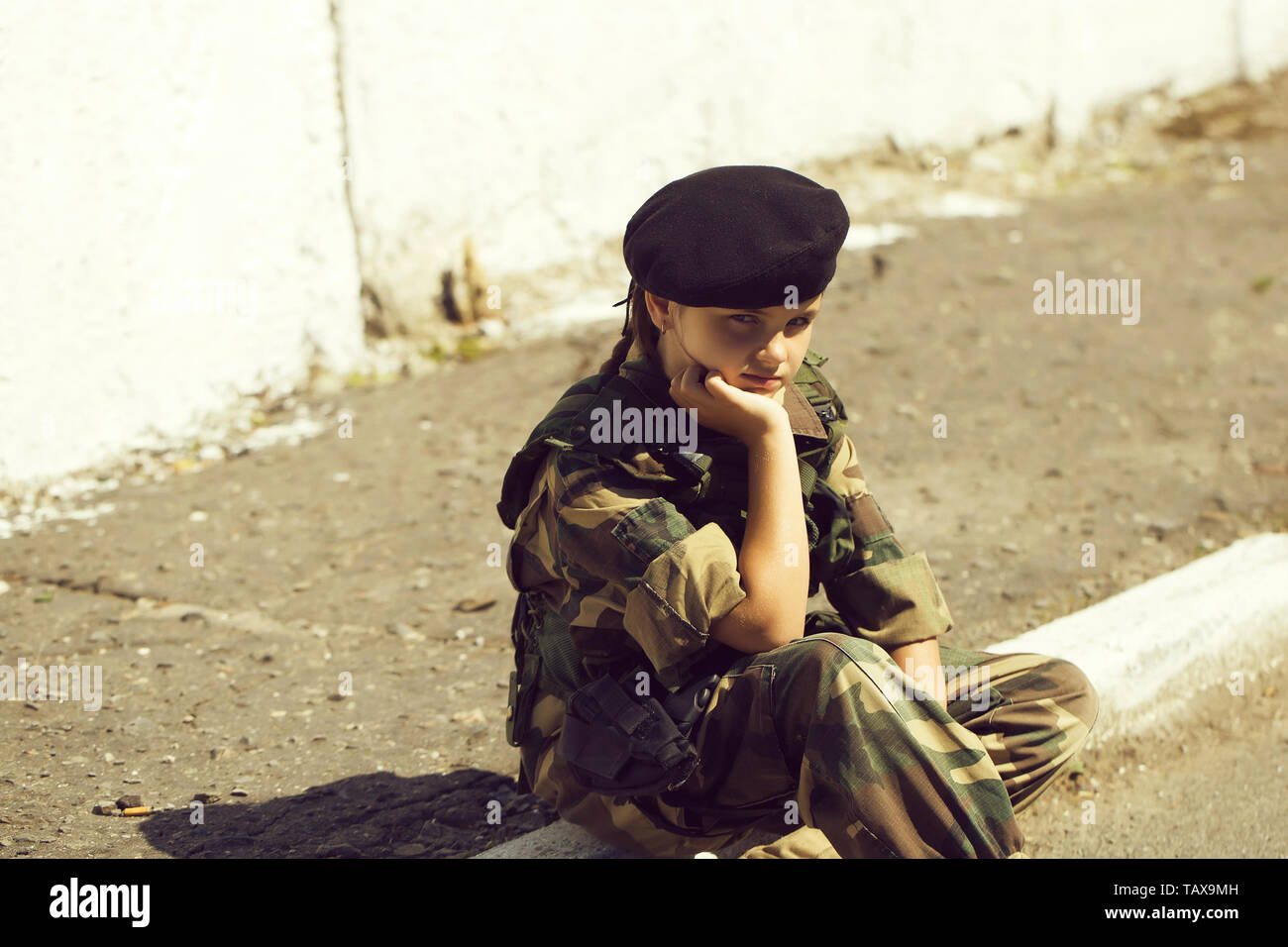 Young girl child with pretty sad thoughtful face in army camouflage  ammunition and black beret sitting on stone ground outdoor Stock Photo -  Alamy
