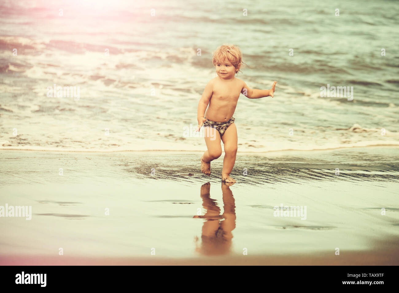 Cute Cheerful Baby Boy With Blond Hair Ponytail In Trunks Runs On