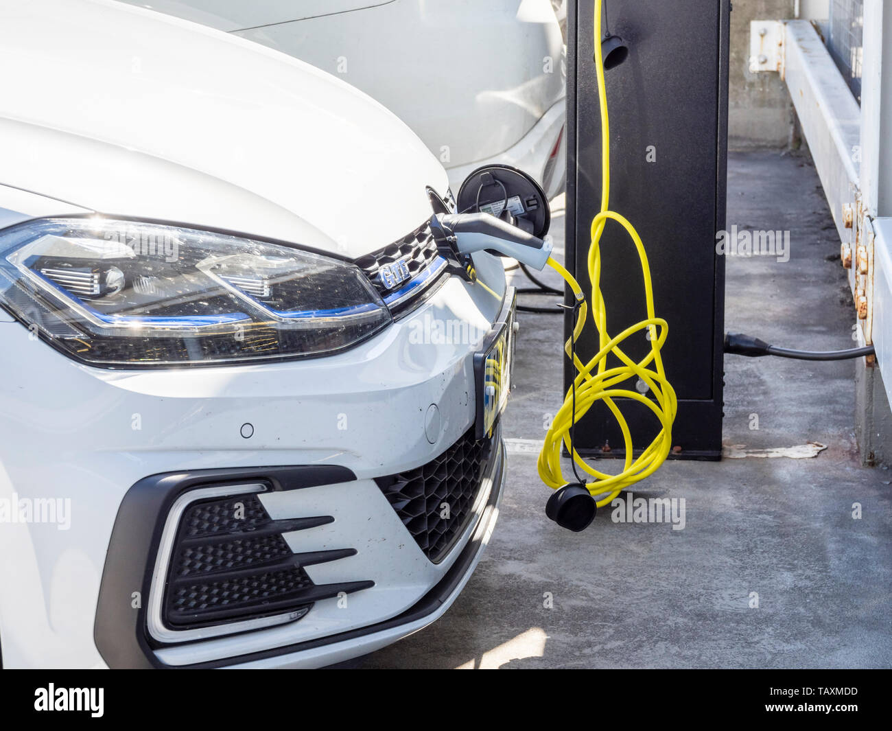 A white electric car connected to a charging point by a yellow cable