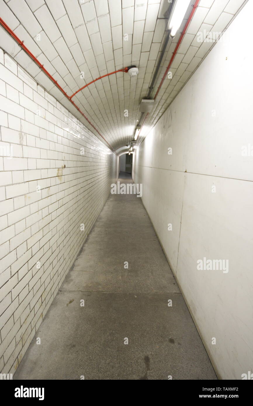 a view along a tile glazed underground foot tunnel with restricted space. The far end of the tunnel disappears in the distance Stock Photo