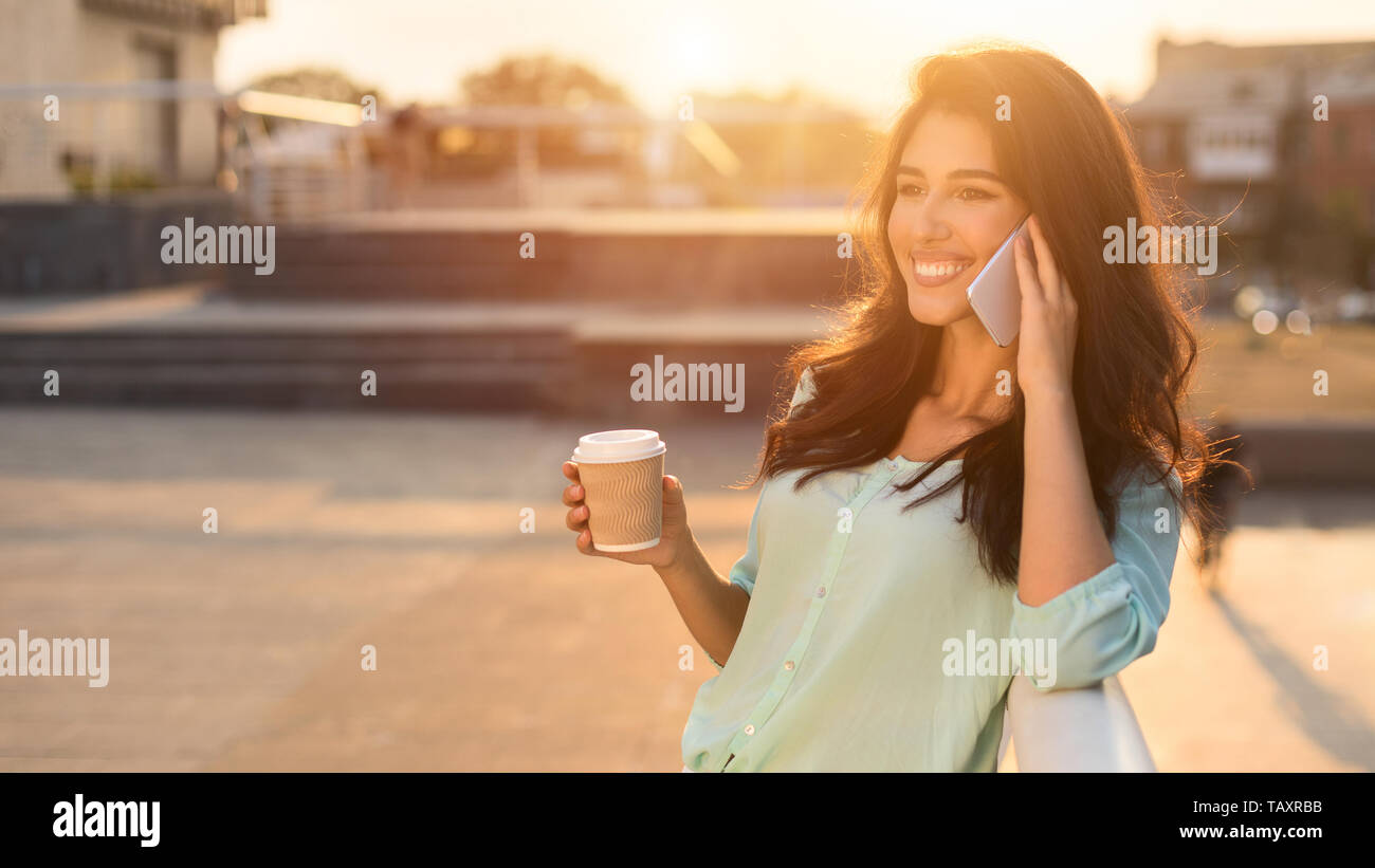 Enjoy free time. Girl talking on phone and drinking coffee in city Stock Photo