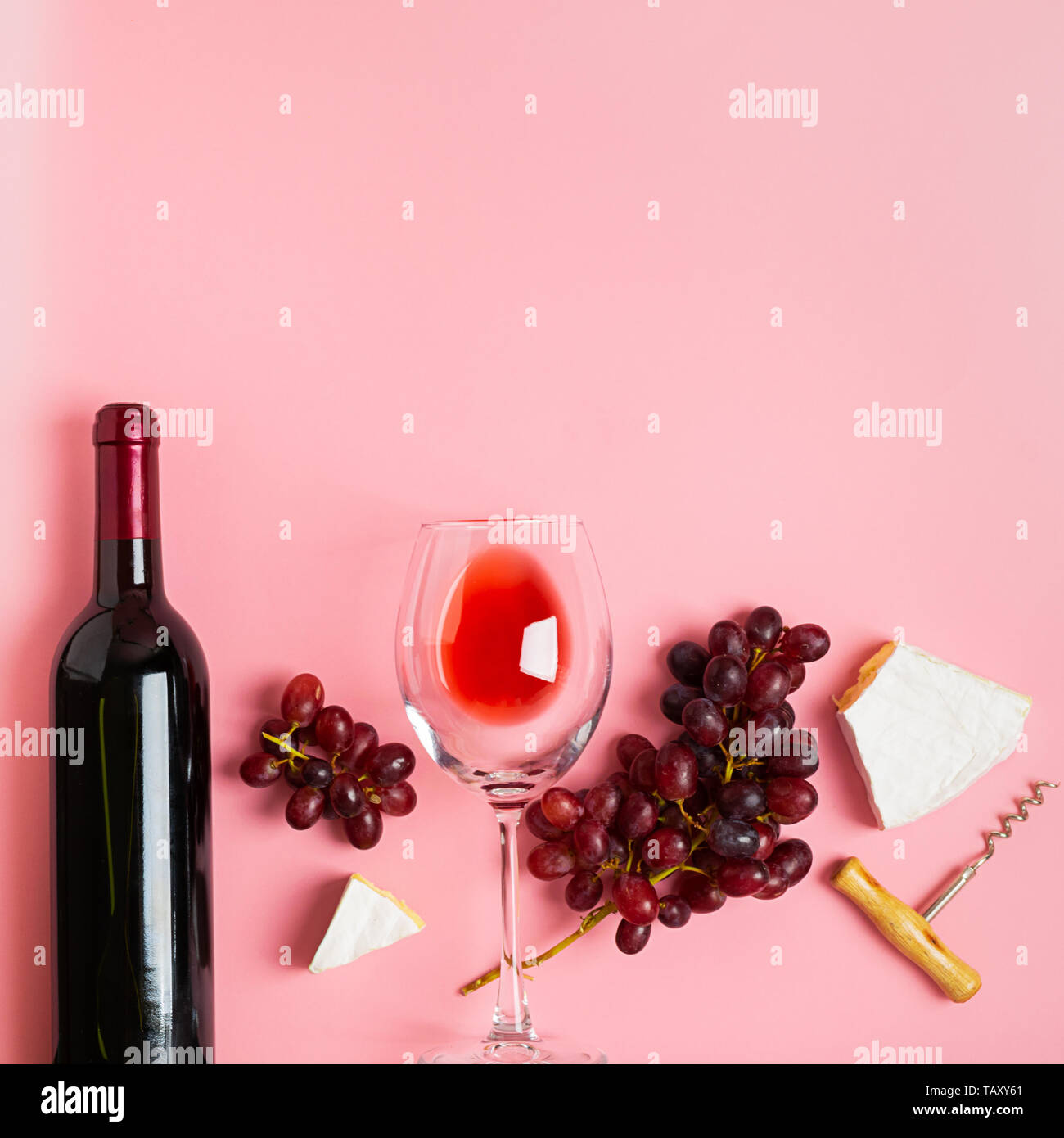 A bottle of wine an empty glass of a bunch of red grapes on a gentle pink background. Flat layout top view. Copy space. Stock Photo