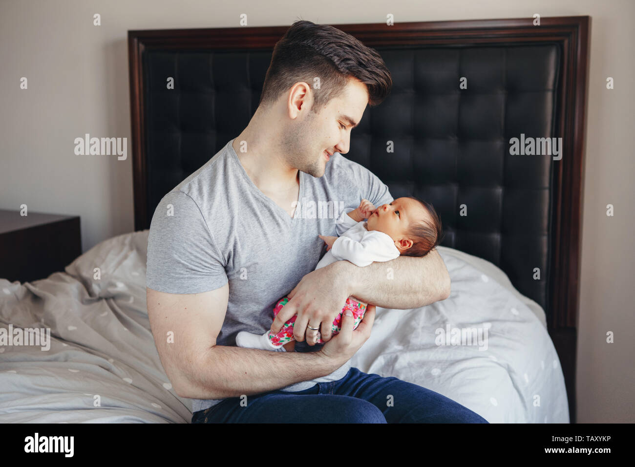 Young Caucasian father dad with his newborn mixed race Asian Chinese baby. Male man parent holding child daughter son. Authentic lifestyle touching te Stock Photo