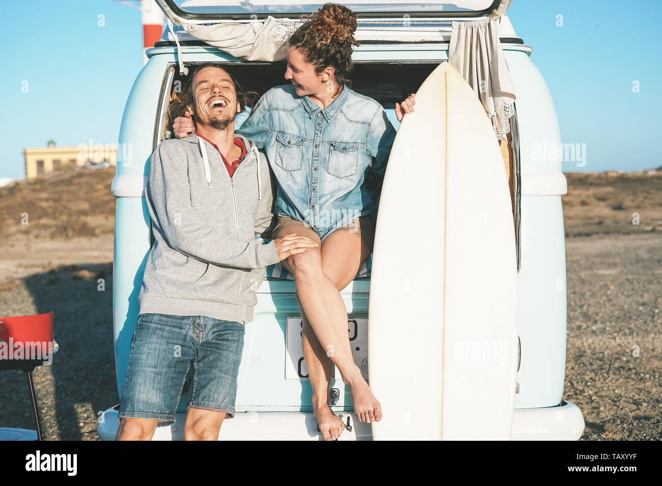 Happy surfers couple standing behind on vintage camper mini van - Young people adventuring on road trip with a minivan transport Stock Photo