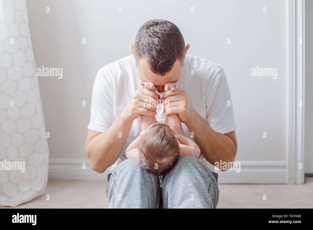 Caucasian father holding newborn baby on laps knees. Male man parent playing with child daughter son feet heels. Authentic lifestyle documenatry funny Stock Photo