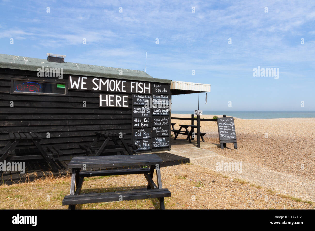 Aldeburgh, Suffolk, UK: On a shingle beach a fish shop with blackboards showing the type of fish for sale on the side of a black wooden shed. Stock Photo