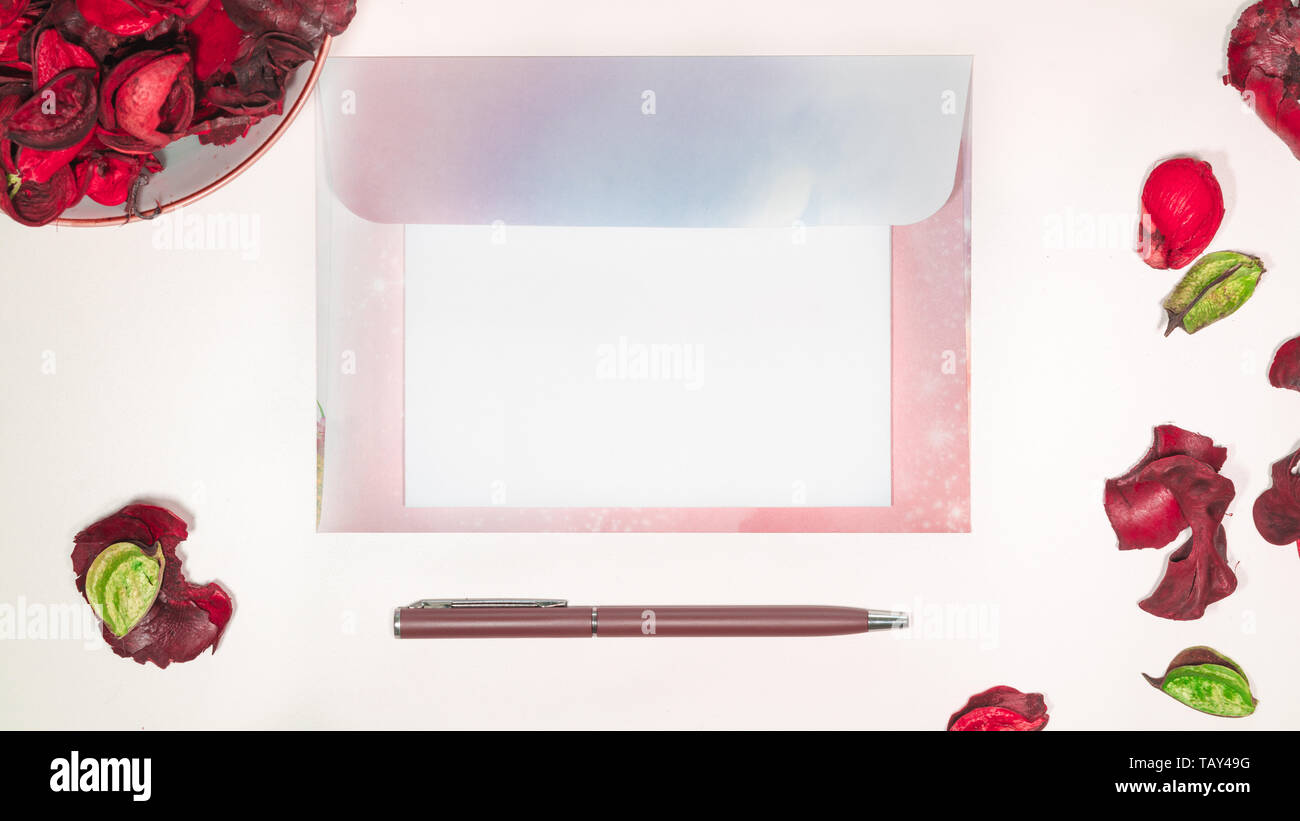 Blank open letter on envelope on a desk with writing supplies and pink dried flowers top view Stock Photo