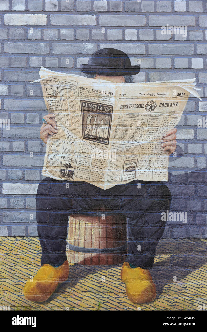 A man with a bowler hat (Derby), suit and wooden clogs reading a newspaper on a beautiful graffiti/wall painting in Zierikzee (Zeeland), Netherlands Stock Photo