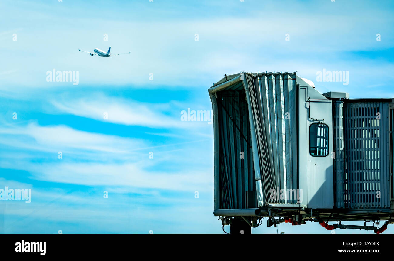 Jet bridge after commercial airline take off at the airport and the plane flying in the blue sky and white clouds. Aircraft passenger boarding bridge  Stock Photo