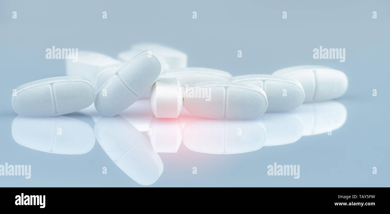 Pile of white oblong tablets pills on gradient background. White antibiotic tablet pills. Pharmaceutical industry. Pharmacy product. Drug in pharmacy  Stock Photo