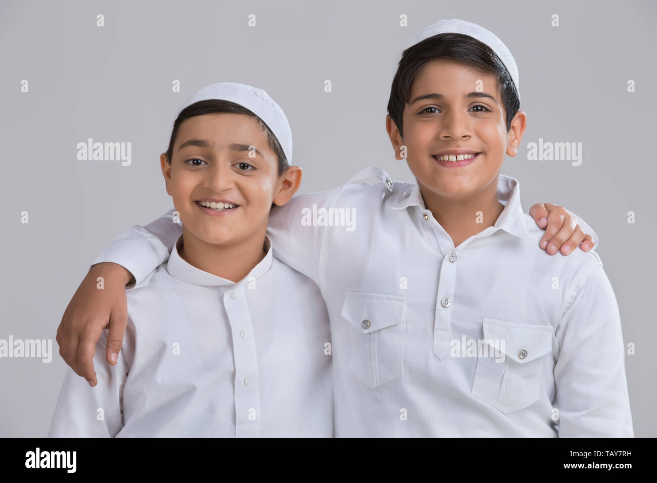 Young Muslim boys with caps smiling and holding each other Stock Photo
