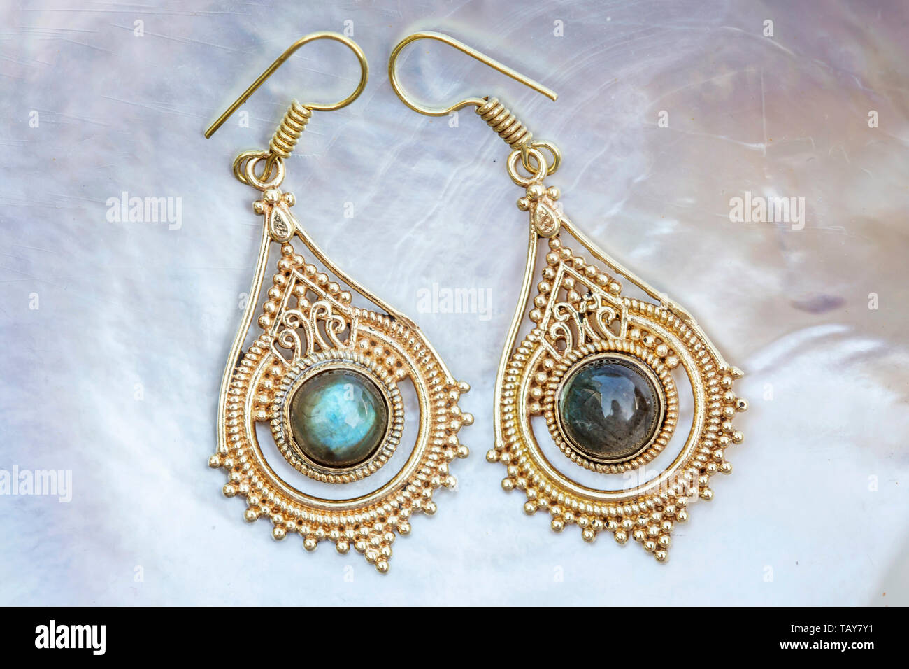 Brass metal earrings with mineral labradorite gemstone on pearl background Stock Photo