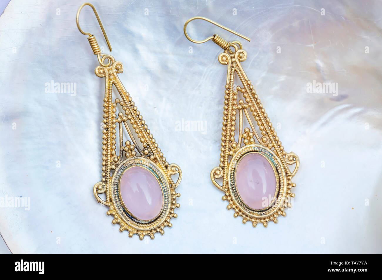 Brass metal earrings with mineral rose quartz gemstone on pearl background Stock Photo