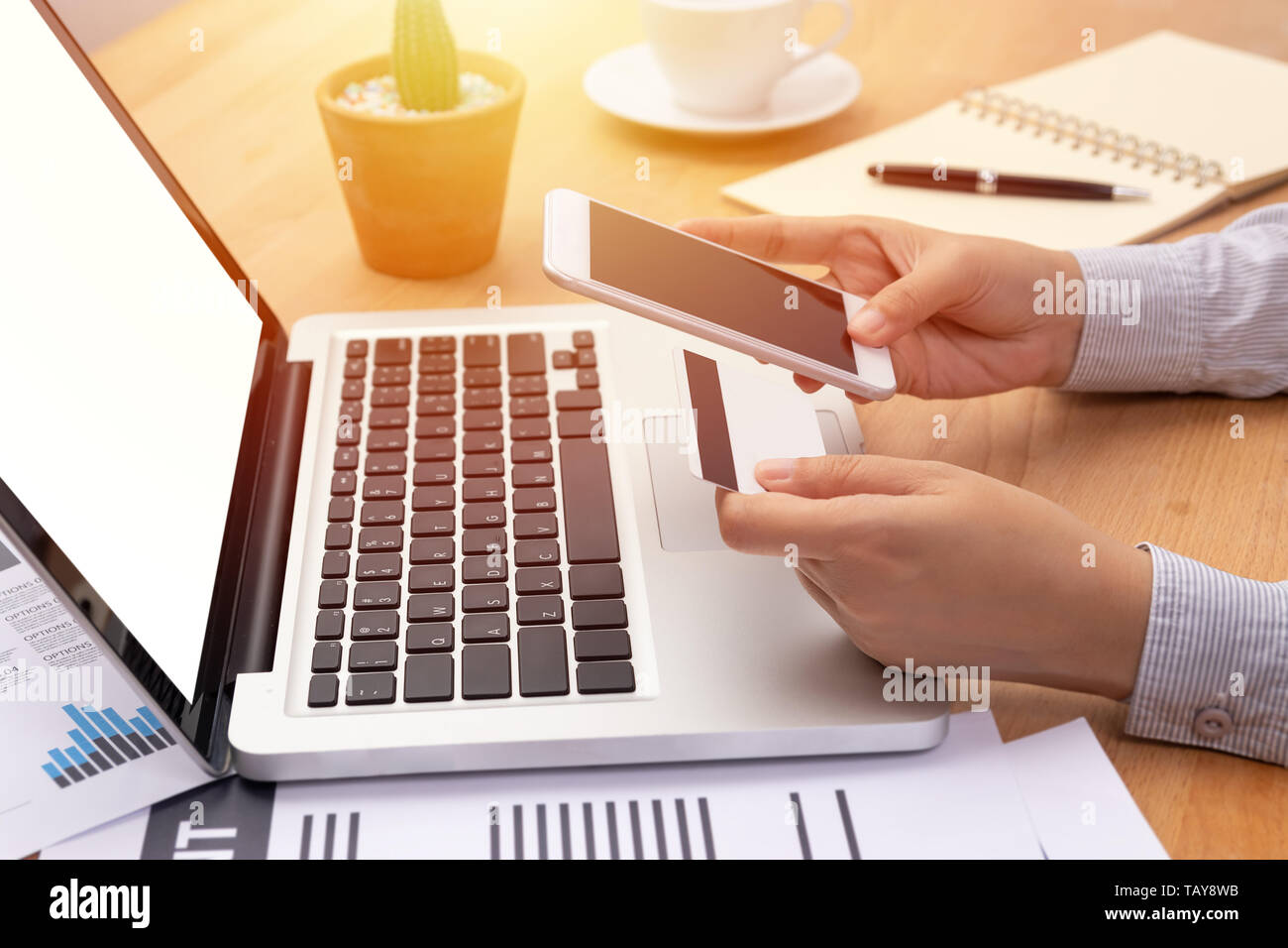 woman holding a credit card and purchase making online payment via mobile smartphone with blank screen in front of computer notebook laptop with blank Stock Photo