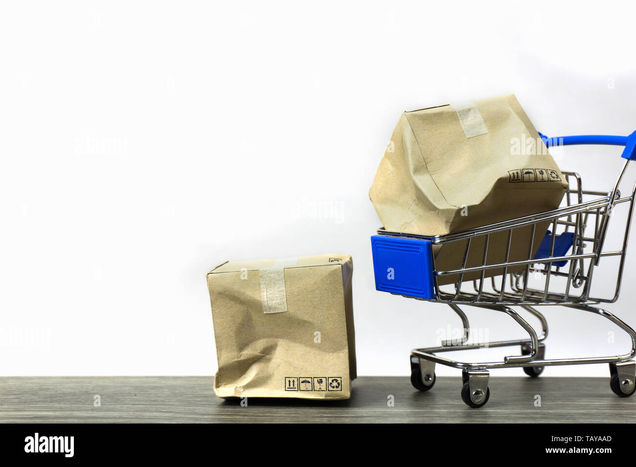Bad delivery concepts. A damaged container box in small blue shopping cart model and on wood table with white background. Depicts transportation of go Stock Photo