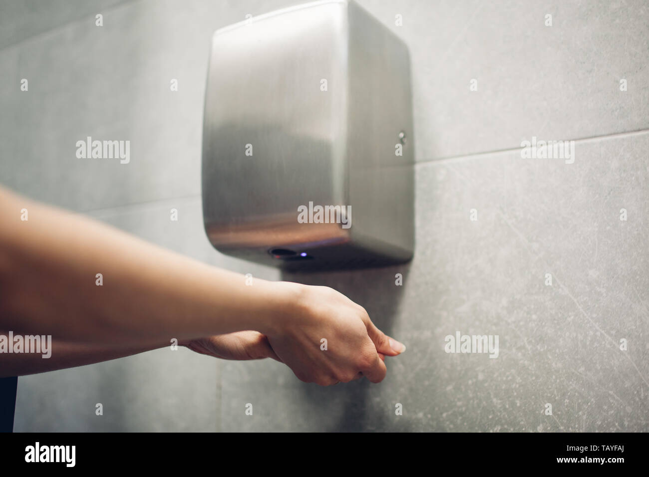 Air dryer in public toilet. Woman drying hands in water closet. Hygiene