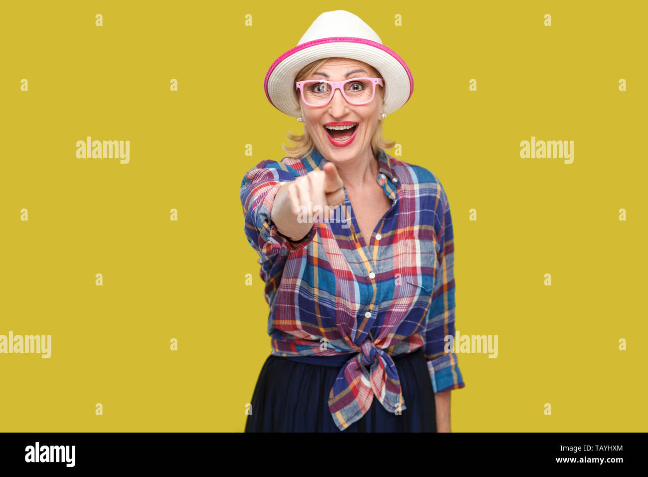 Portrait of funny surprised modern stylish mature woman in casual style with hat and eyeglasses standing, looking and pointing at camera with amazed f Stock Photo