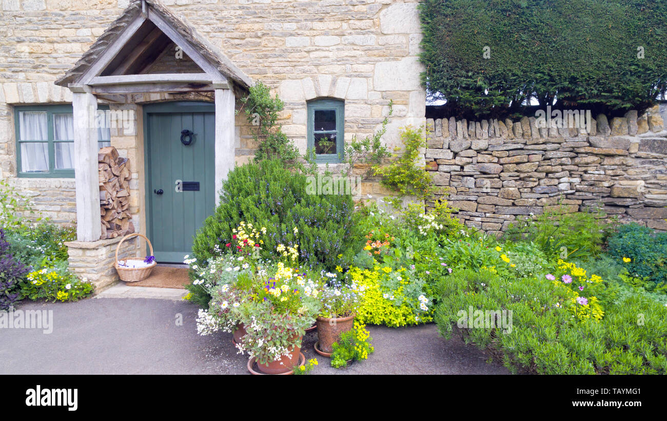 Front garden with vibrant flowers in bloom, lush herbs by a stone cottage in an english rural village. Stock Photo