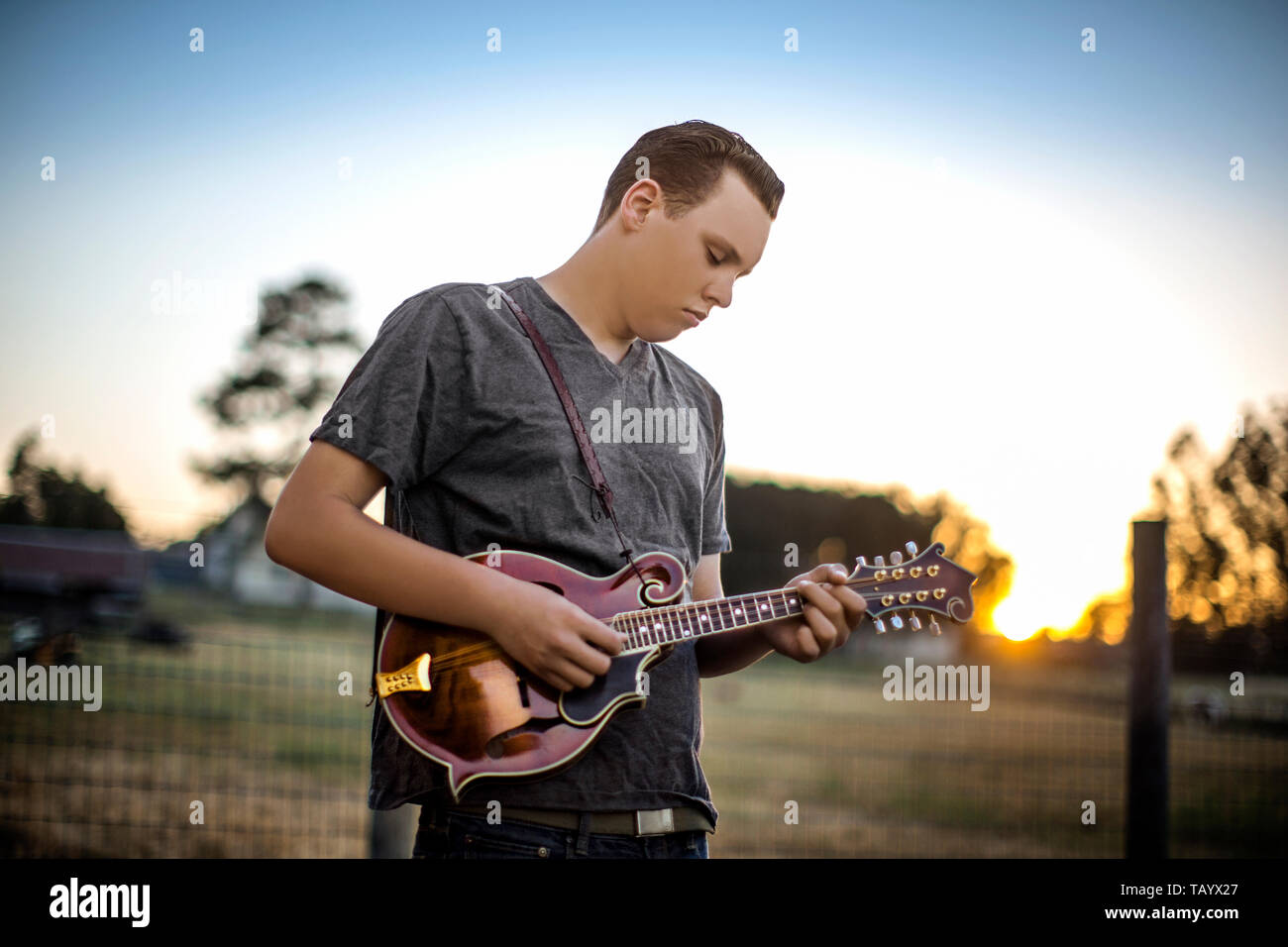 Contented teenage boy playing a mandolin in a rural field. Stock Photo