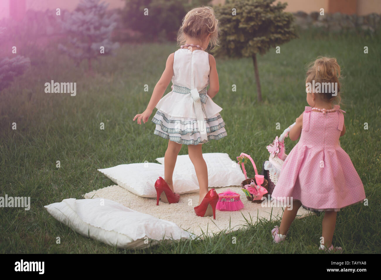 Girl in red mothers shoes on high heels on summer day. Sisters in stylish  dresses play on green grass lawn. Fashion, style, beauty. Vacation, leisure  Stock Photo - Alamy