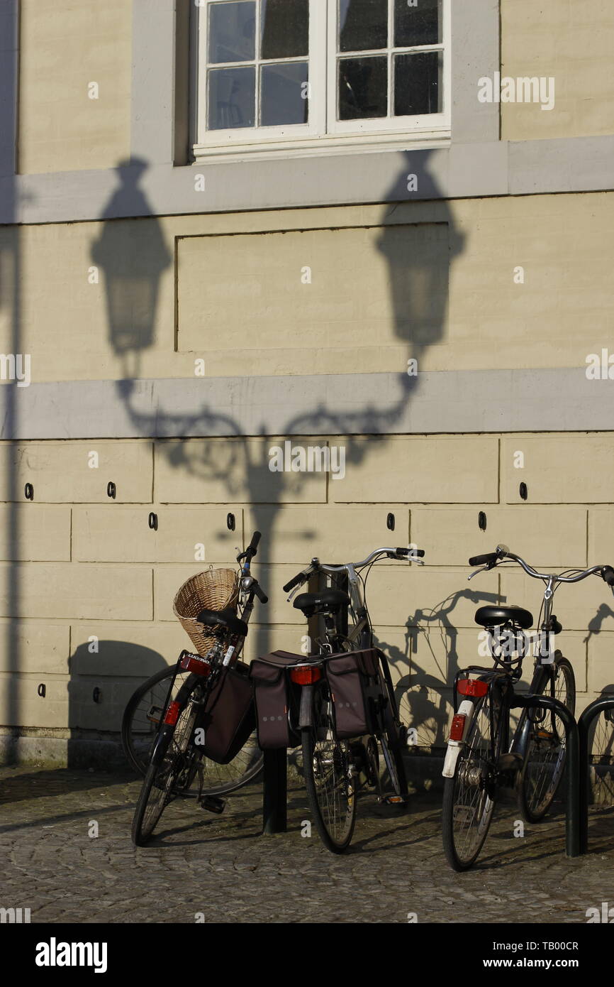 image showing a collection of parked bicycles against a wall with a shadow of a lampost giving the illusion that the bikes are supprted by the shadow Stock Photo