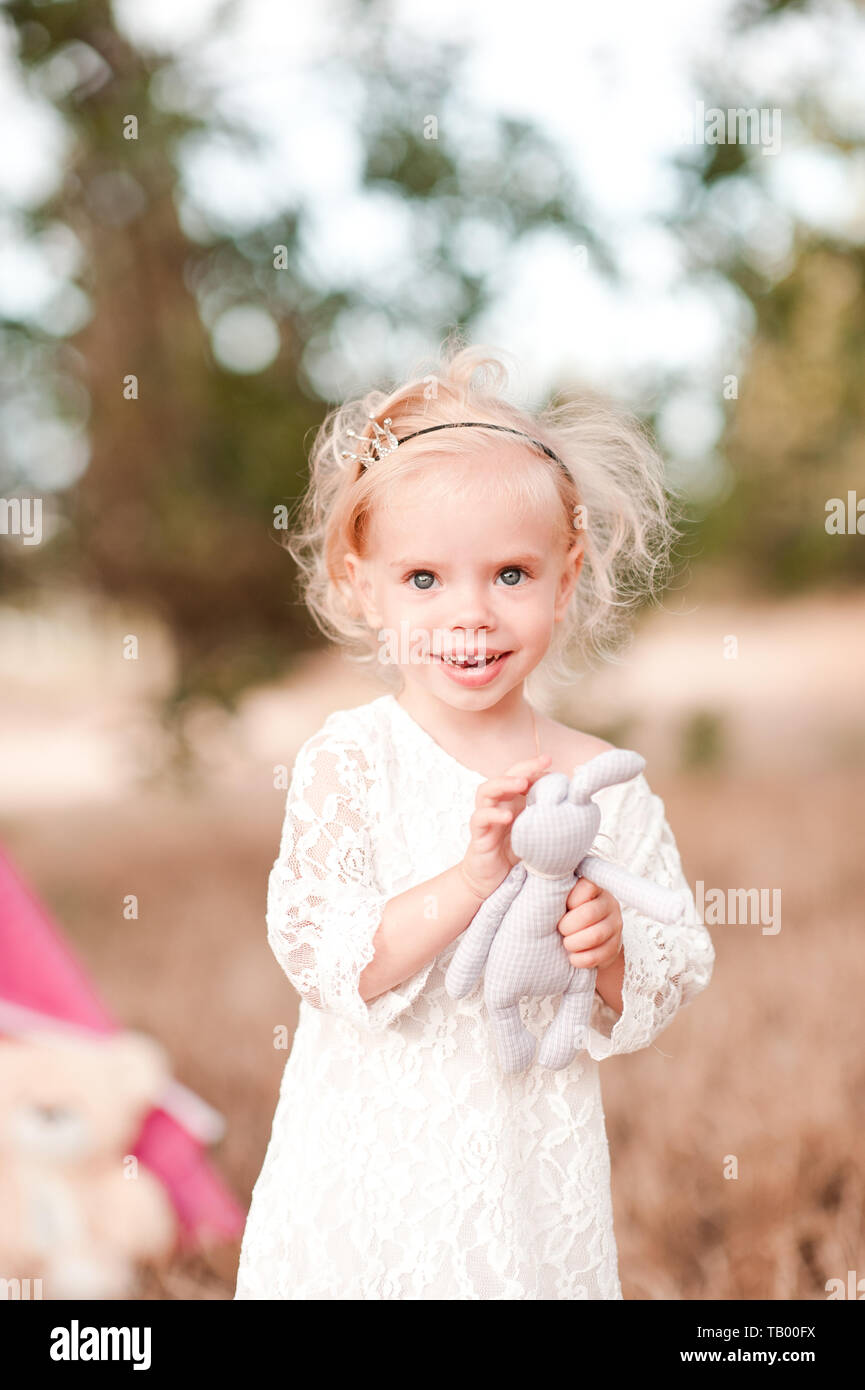 Smiling baby girl 1-2 year old holding toy rabbit outdoors. Looking at camera. Childhood. Happiness. Stock Photo