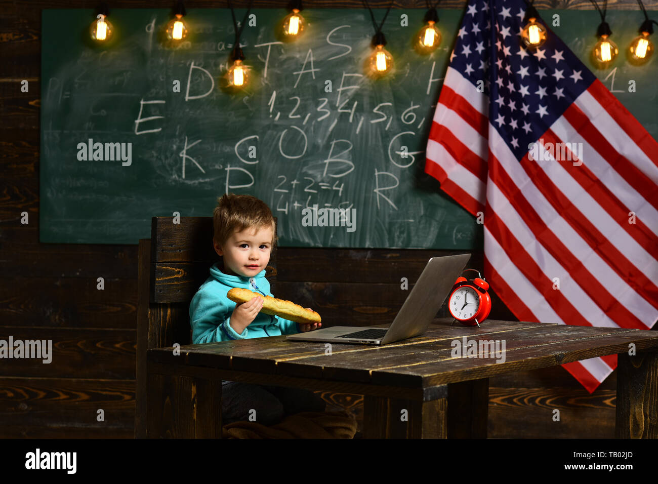 kid with computer in elementary school on the USA national flag background. Pupil on the background with flag of the USA Stock Photo