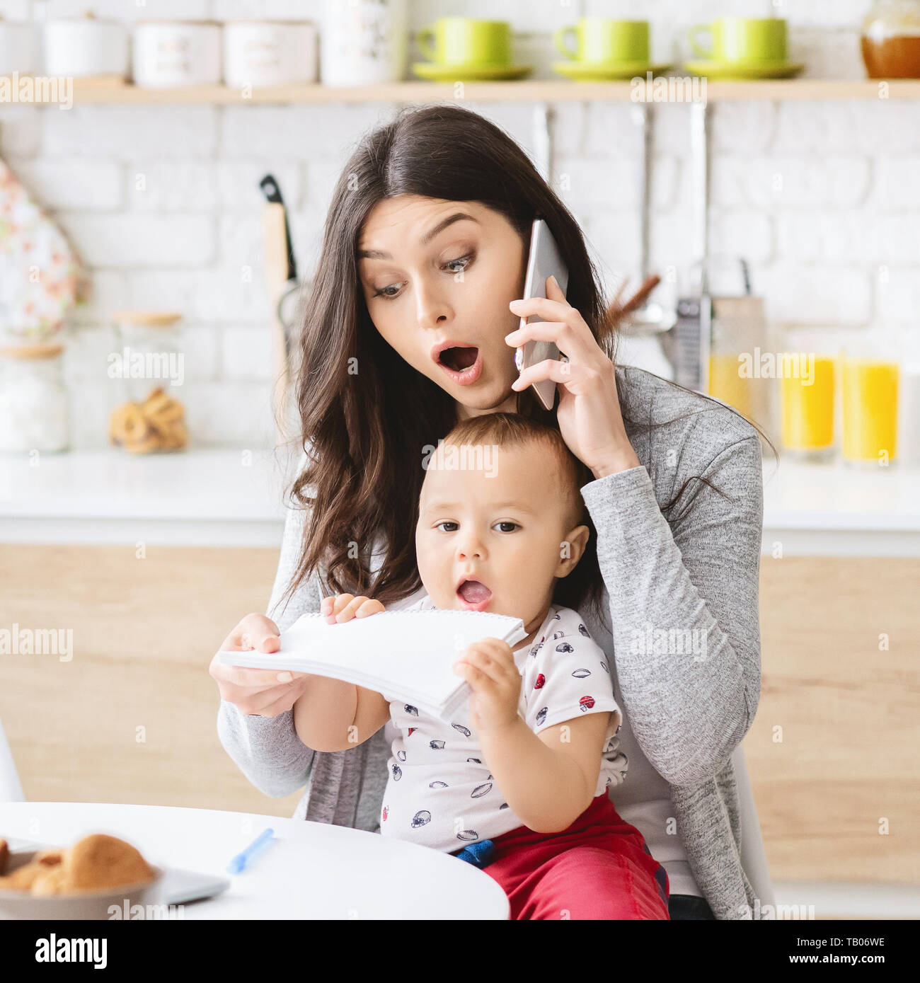 Business mom talking on phone and taking notes from baby hands Stock Photo