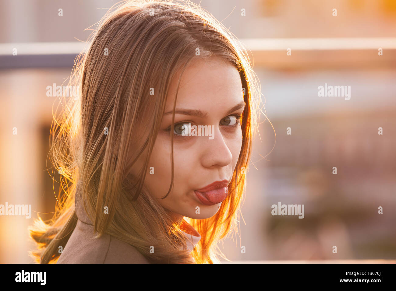 Beautiful European teenage girl shows tongue, close up outdoor portrait with back-lit sunlight Stock Photo