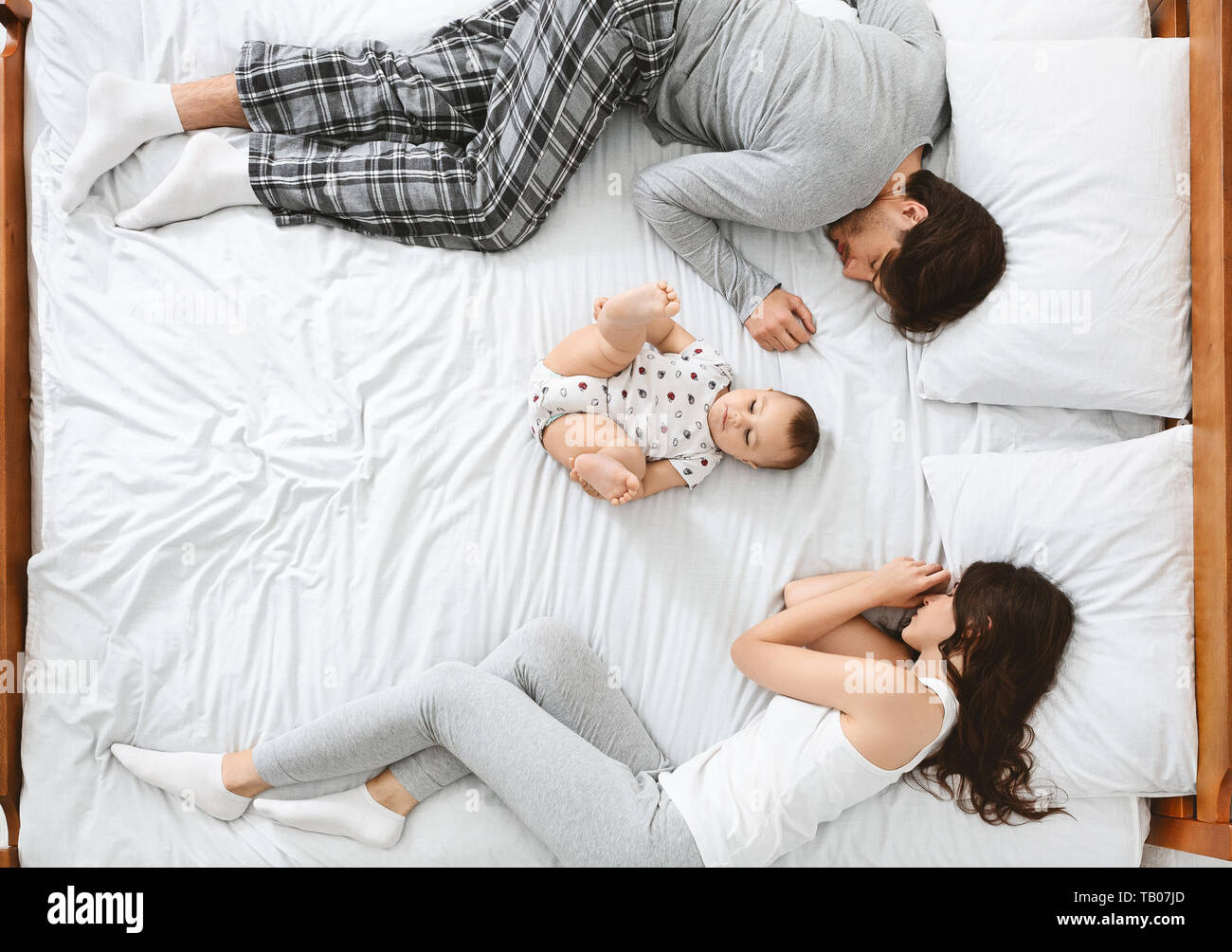 Little baby lying in the middle of bed, parents sleeping on sides Stock Photo