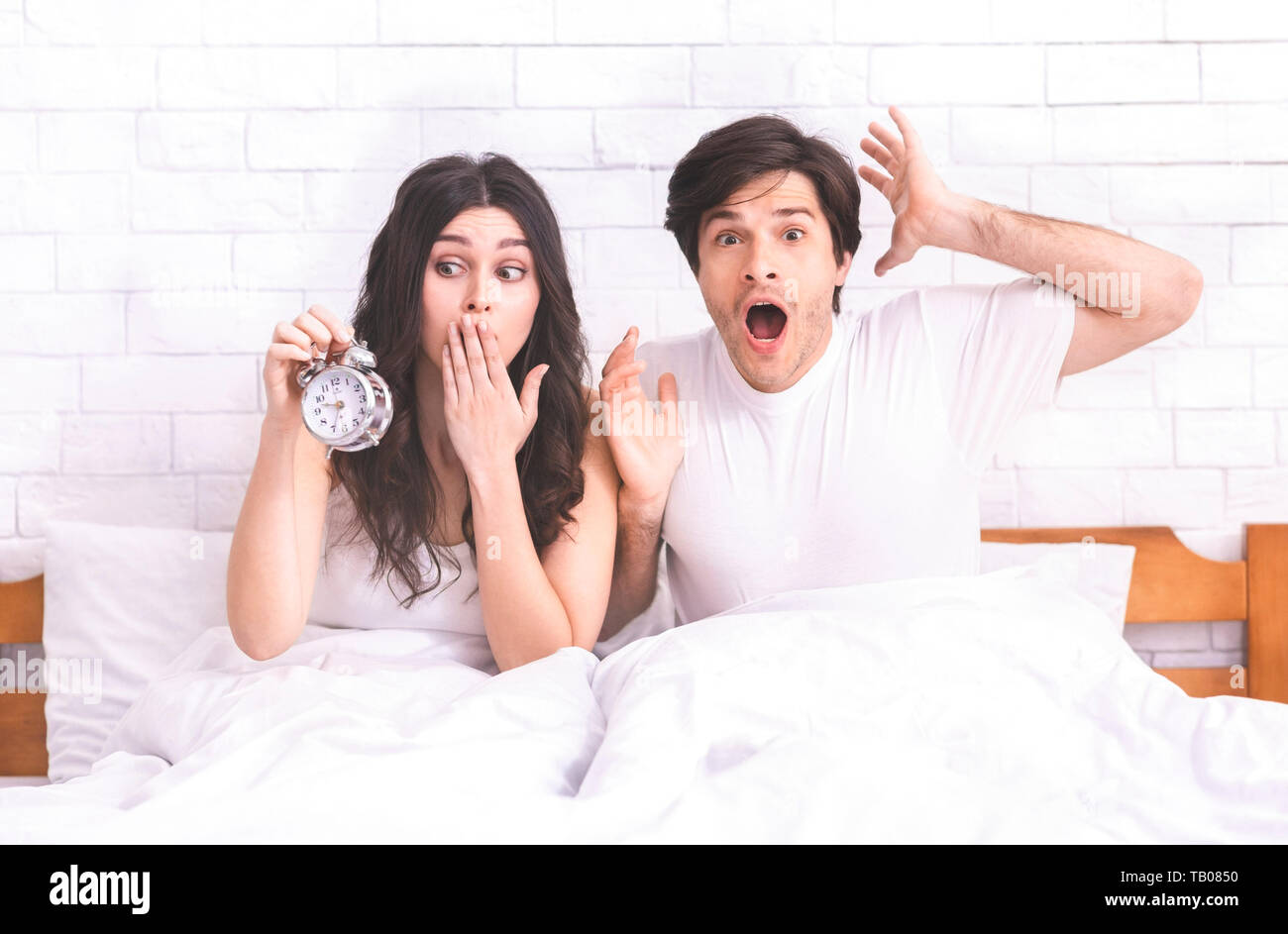 Confused couple missed ringing of alarm clock in bed Stock Photo