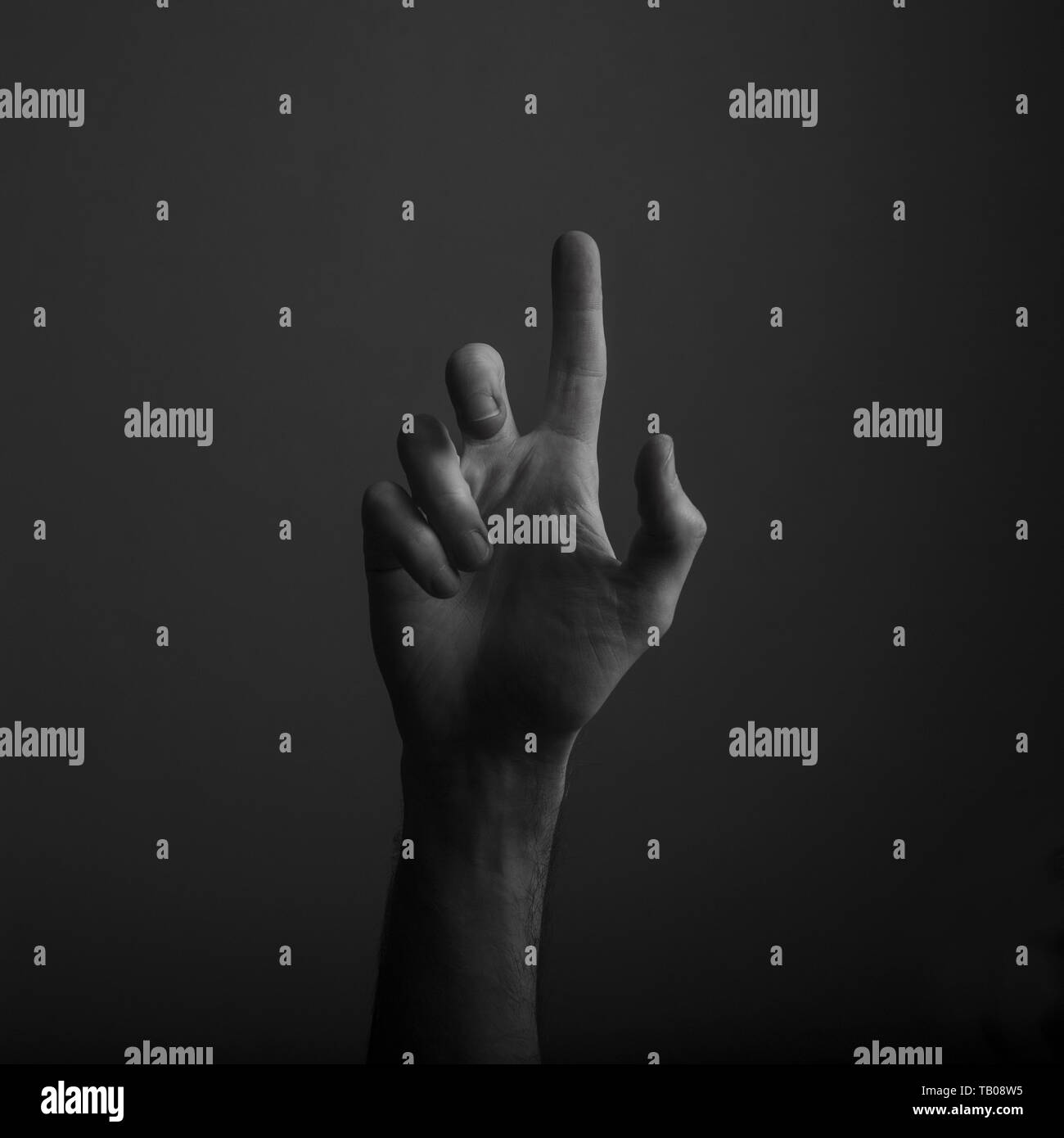 Male hand pointing a finger against a dark background. Selecting, touching Stock Photo
