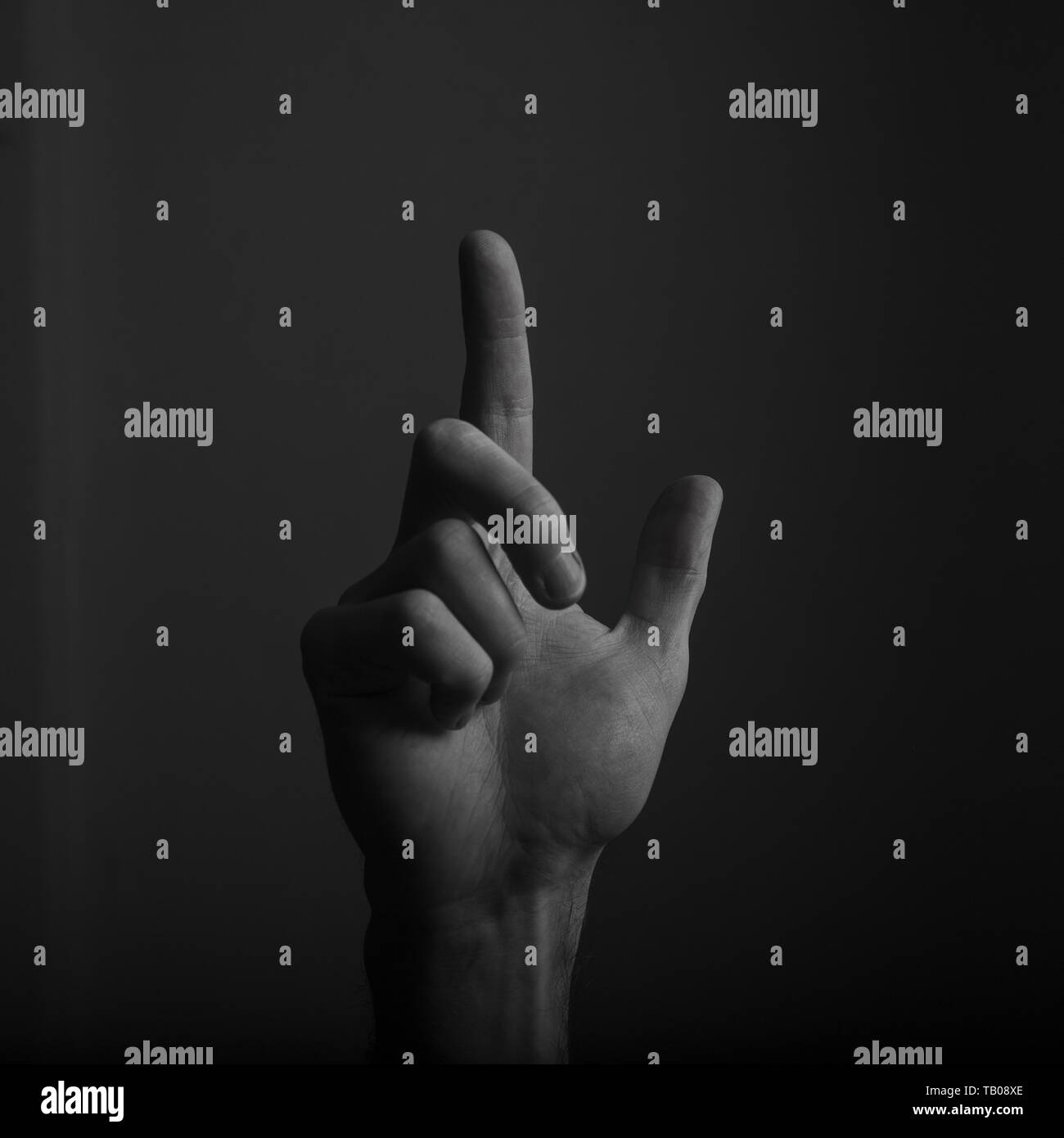 Male hand pointing a finger against a dark background. Selecting, touching Stock Photo