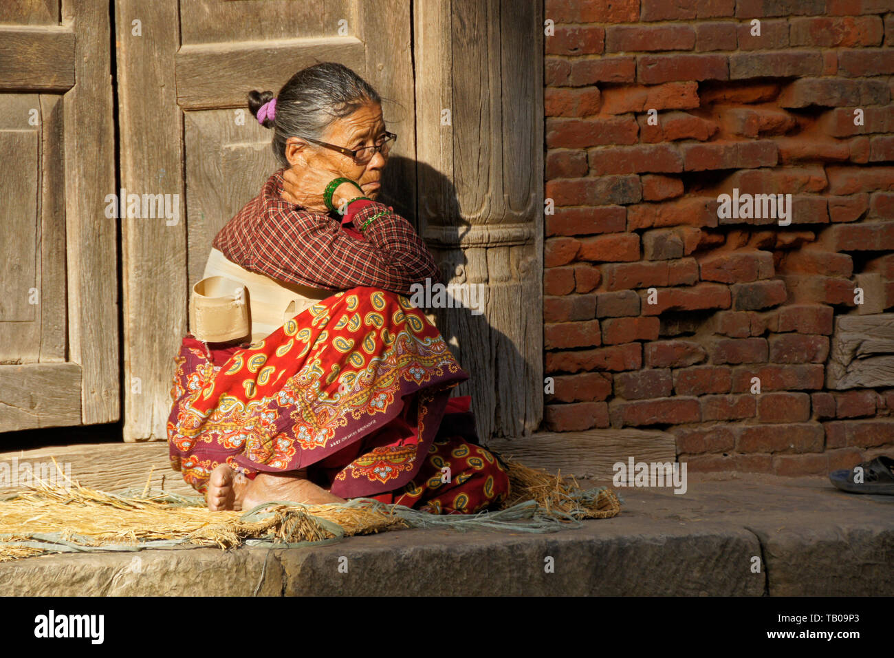Elderly women (wearing back brace) sitting in sun on stoop of home in old town Dhulikhel, Nepal