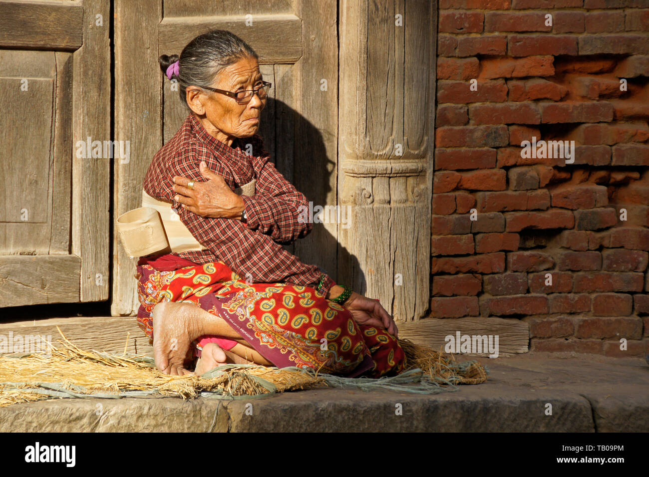 Elderly women (wearing back brace) sitting in sun on stoop of home in old town Dhulikhel, Nepal
